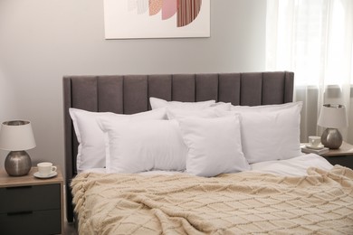 Photo of Many soft white pillows and knitted blanket on bed indoors