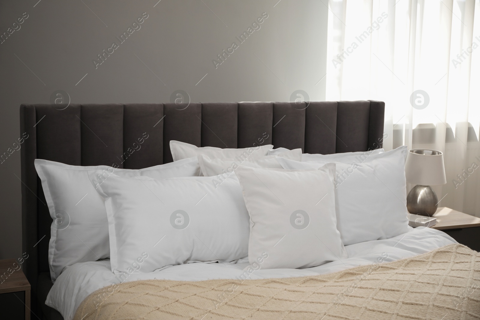 Photo of Many soft white pillows and knitted blanket on bed indoors