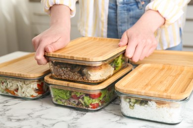 Photo of Healthy food. Woman closing glass container with meal at white marble table, closeup