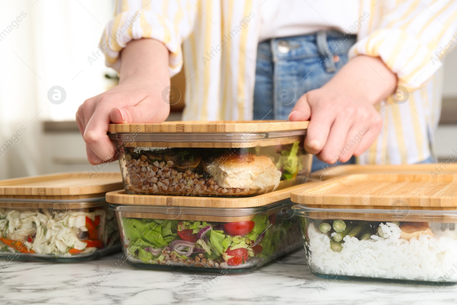 Photo of Healthy food. Woman closing glass container with meal at white marble table, closeup