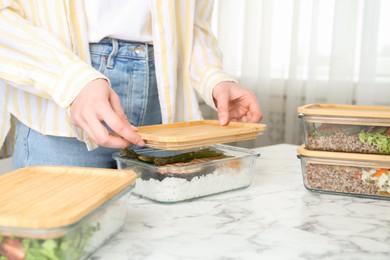 Photo of Healthy food. Woman closing glass container with meal at white marble table, closeup