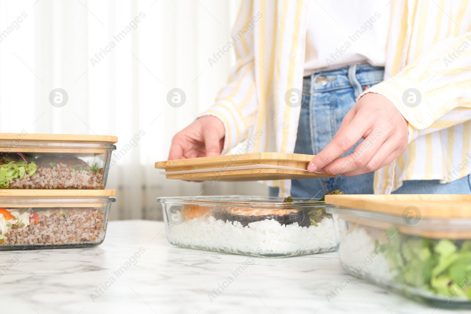 Photo of Healthy food. Woman closing glass container with meal at white marble table, closeup