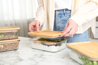 Healthy food. Woman closing glass container with meal at white marble table, closeup