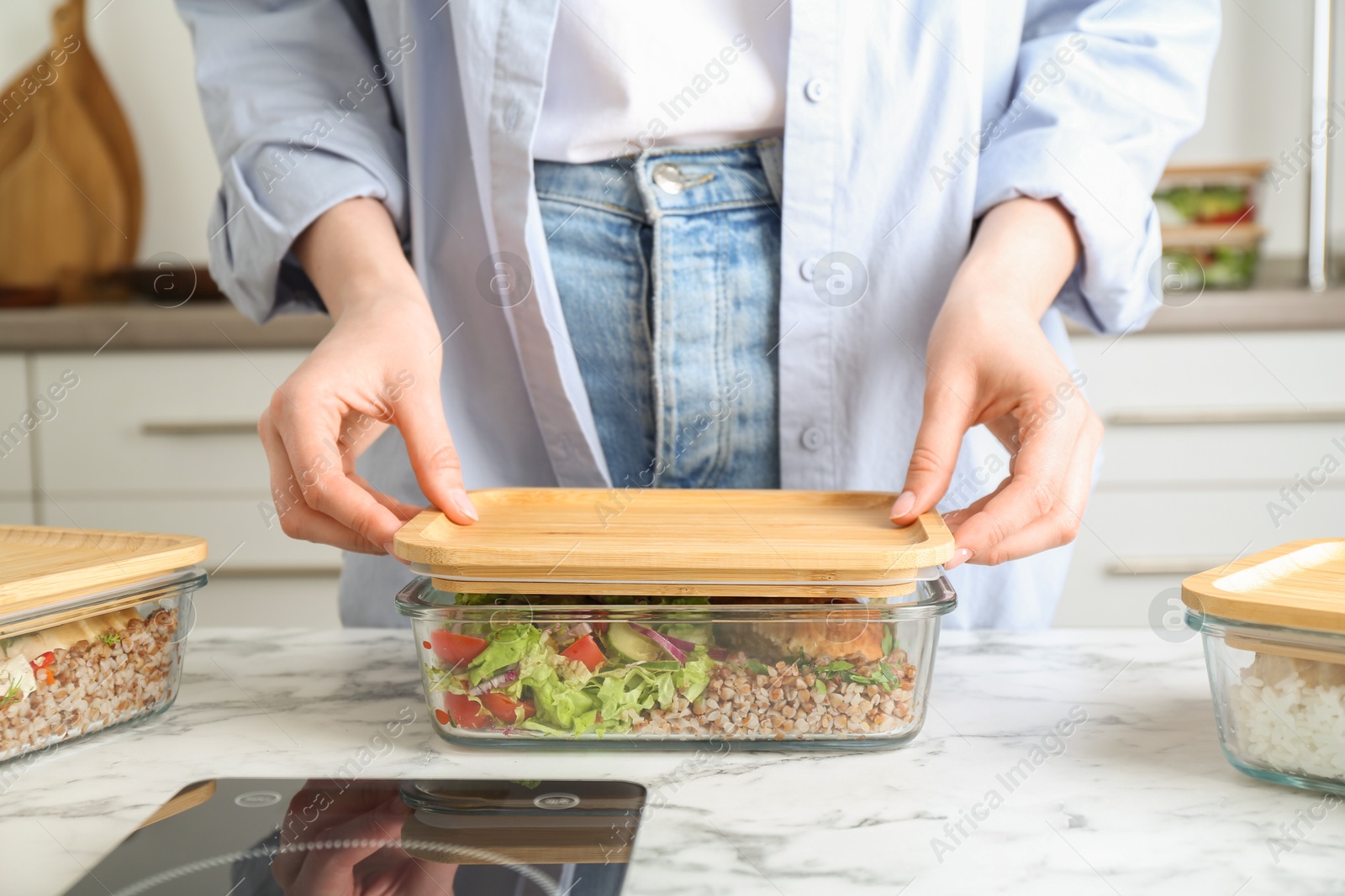 Photo of Healthy food. Woman closing glass container with meal at white marble table, closeup