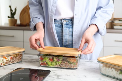 Photo of Healthy food. Woman closing glass container with meal at white marble table, closeup