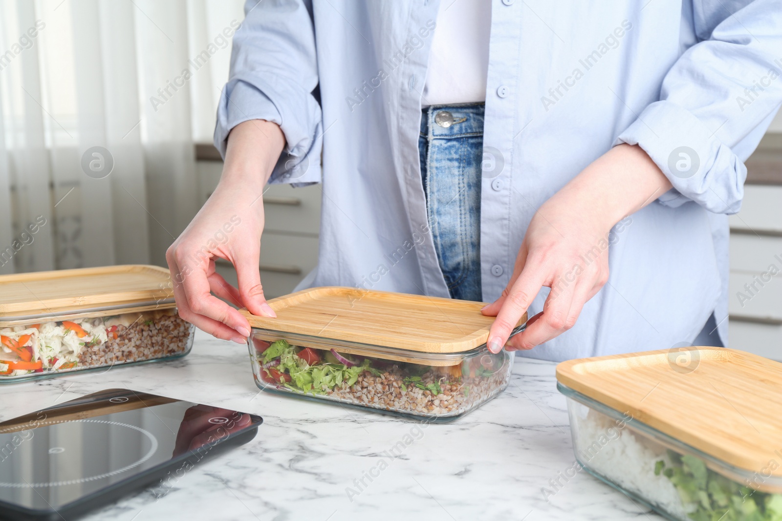 Photo of Healthy food. Woman closing glass container with meal at white marble table, closeup