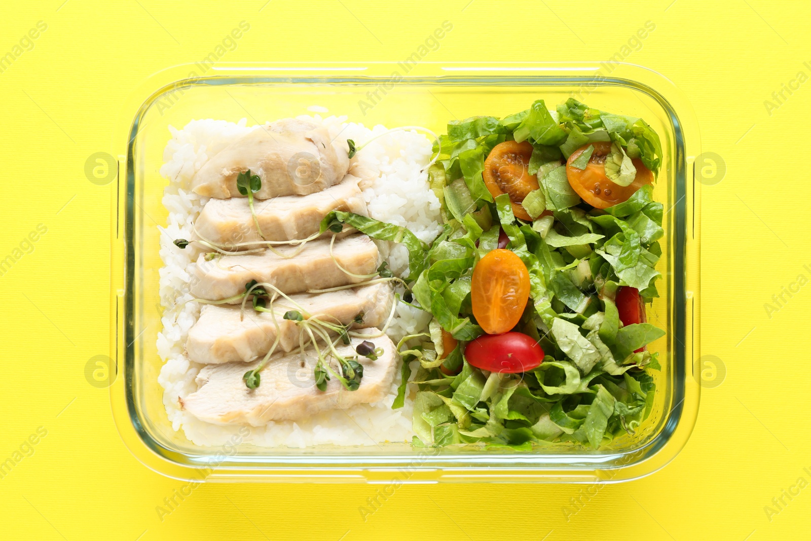 Photo of Healthy meal. Fresh salad, chicken and rice in glass container on yellow background, top view