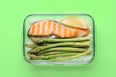 Photo of Healthy meal. Fresh asparagus, salmon, rice and lemon in glass container on green background, top view