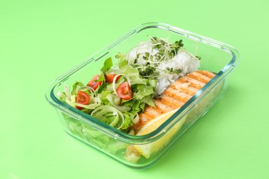 Healthy meal. Fresh salad, salmon and rice in glass container on green background