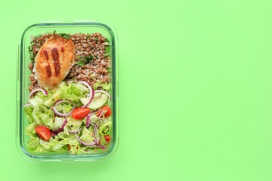 Photo of Healthy meal. Fresh salad, cutlet and buckwheat in glass container on green background, top view. Space for text