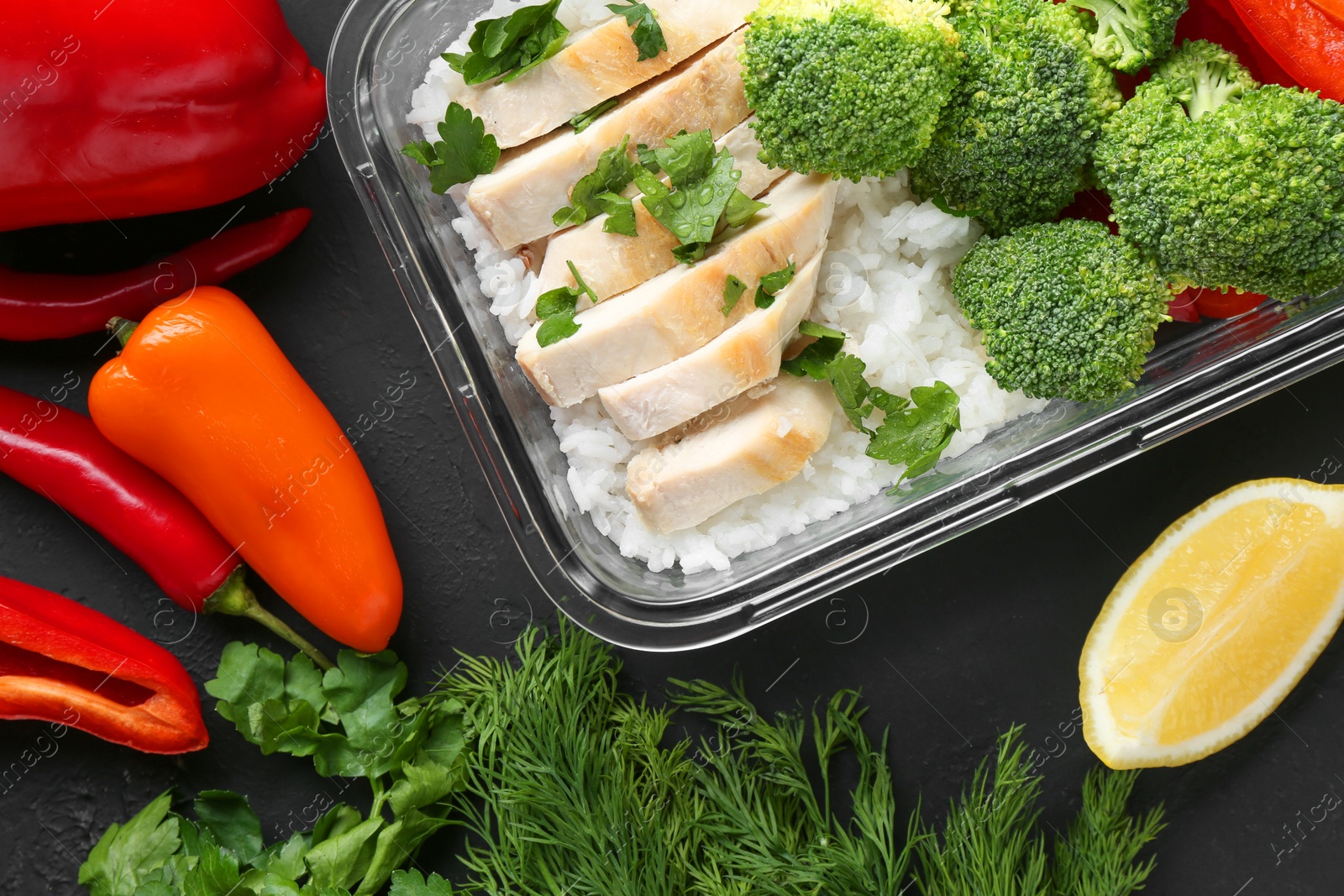 Photo of Healthy meal. Fresh broccoli, chicken and rice in glass container near other products on black table, flat lay