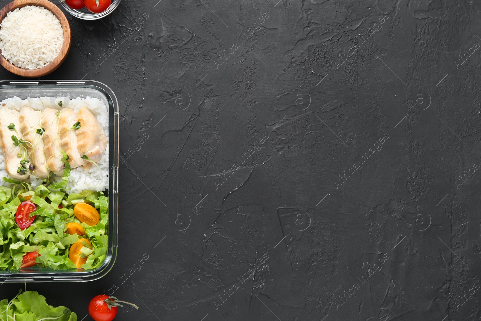 Photo of Healthy meal. Fresh salad, chicken and rice in glass container near other products on black table, top view. Space for text