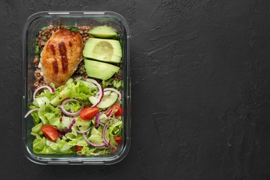 Photo of Healthy meal. Fresh salad, avocado, cutlet and buckwheat in glass container on black table, top view. Space for text