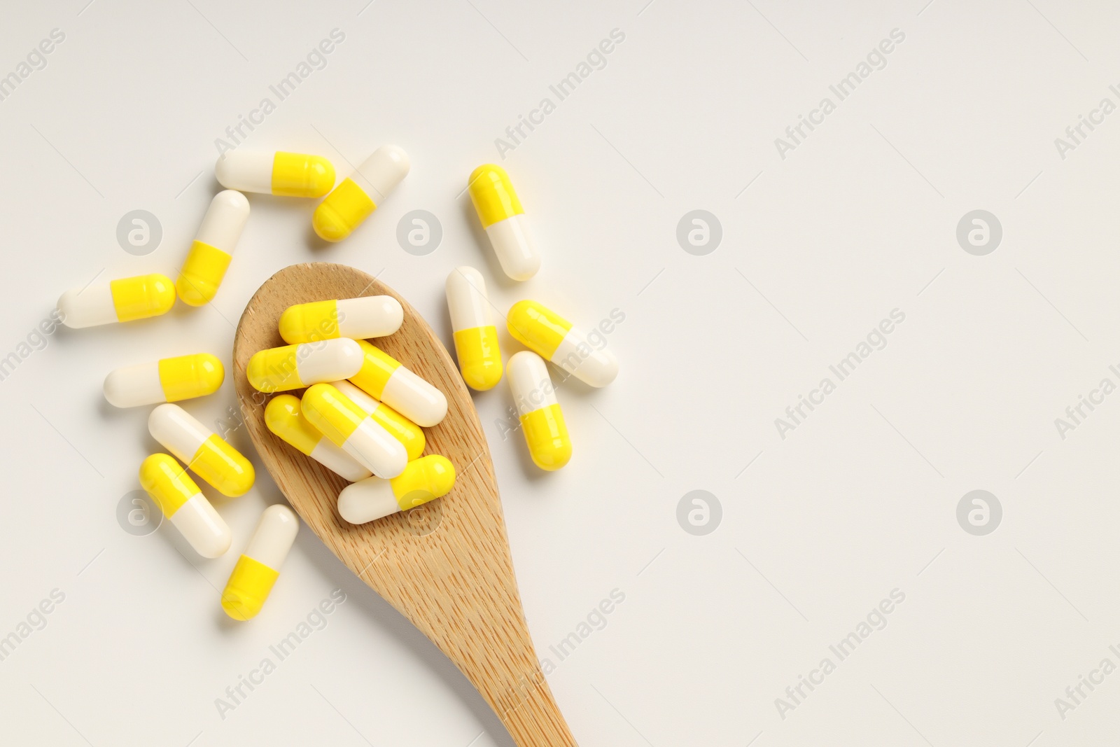 Photo of Antibiotic pills and spoon on white background, top view. Space for text