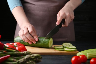 Healthy food. Woman cutting cucumber at black wooden table, closeup