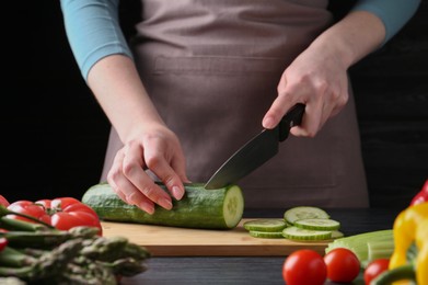 Photo of Healthy food. Woman cutting cucumber at black wooden table, closeup