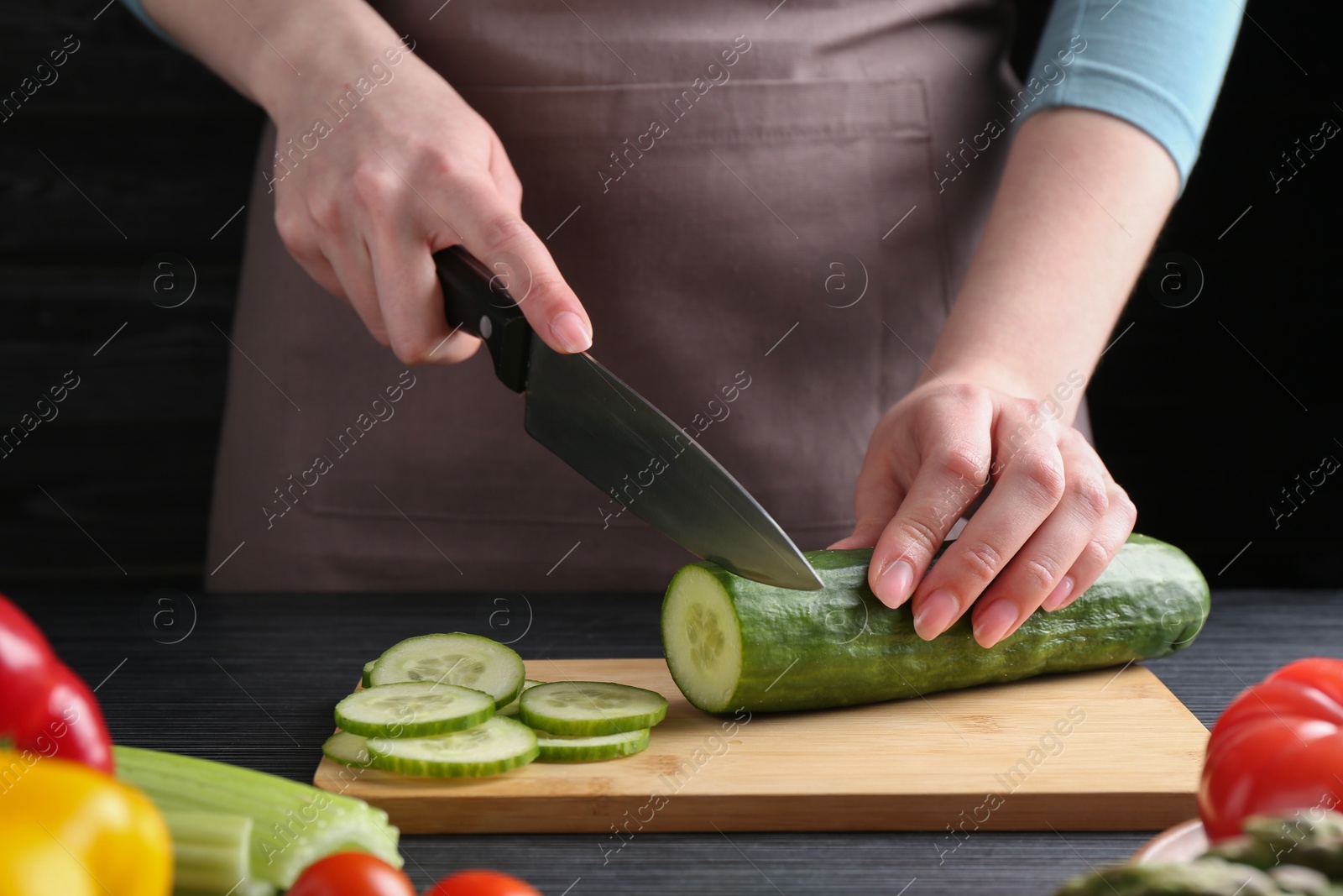 Photo of Healthy food. Woman cutting cucumber at black wooden table, closeup