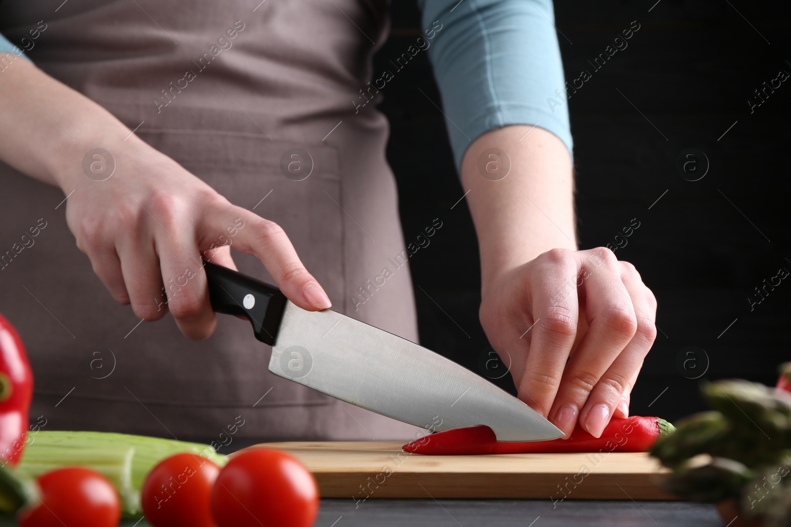 Photo of Healthy food. Woman cutting chili pepper at black wooden table, closeup