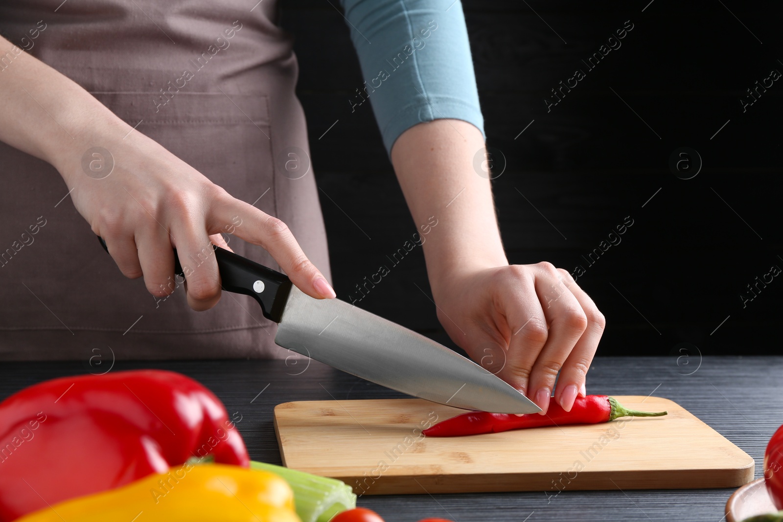 Photo of Healthy food. Woman cutting chili pepper at black wooden table, closeup