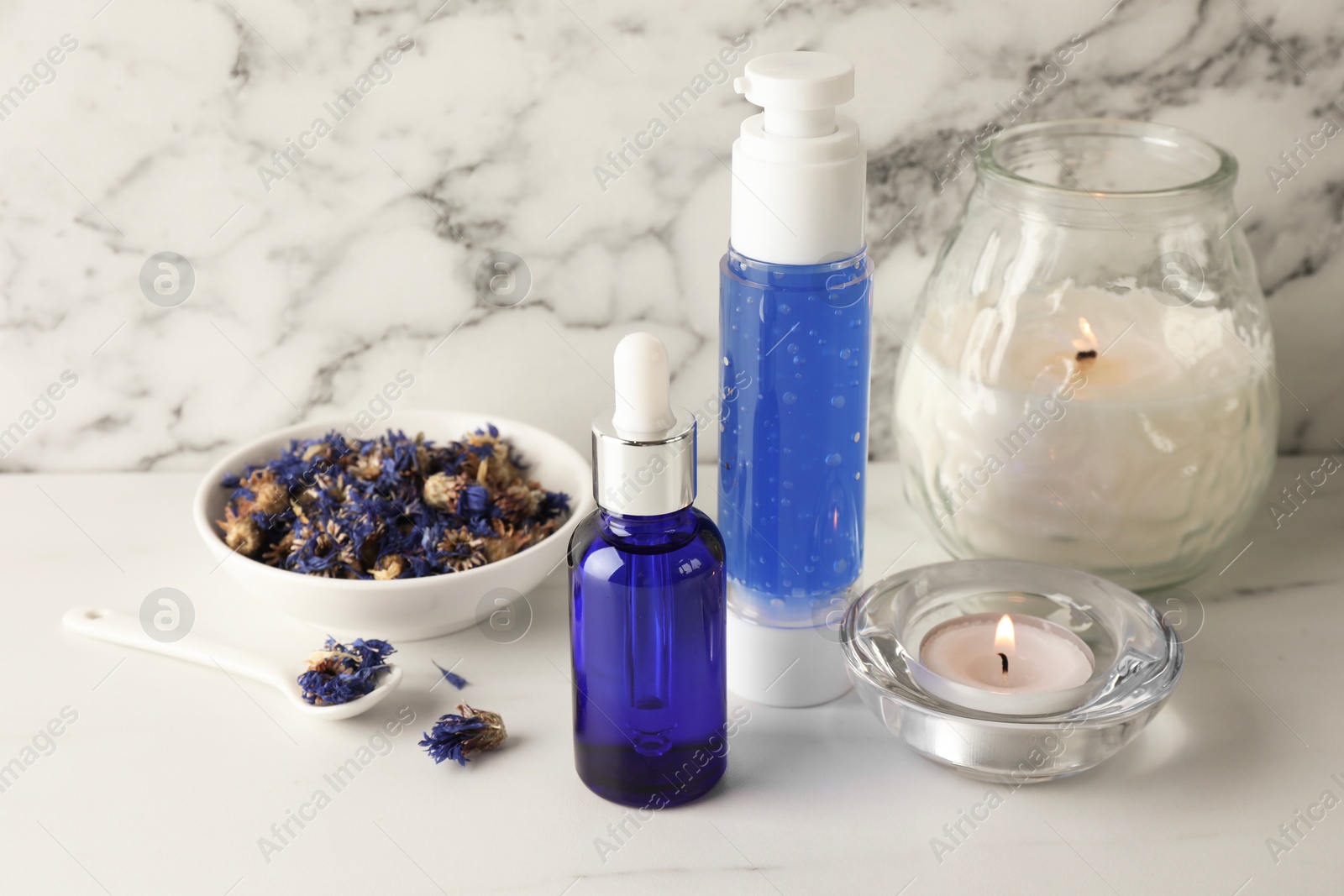 Photo of Spa composition. Bottles of cosmetic products, dry flowers and burning candles on white marble table