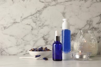 Photo of Spa composition. Bottles of cosmetic products, dry flowers and burning candles on white marble table, space for text