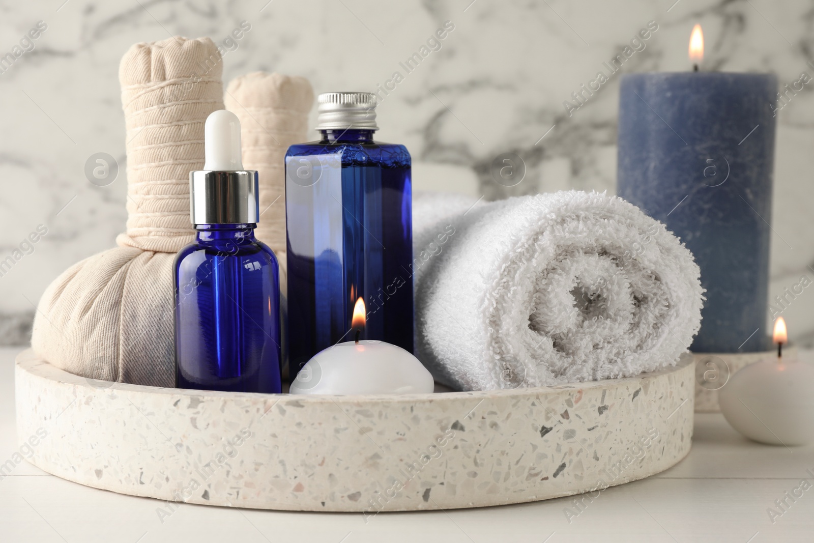 Photo of Spa composition. Bottles of cosmetic products, towel, herbal bags and burning candles on white wooden table