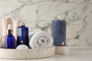 Spa composition. Bottles of cosmetic products, towel, herbal bags and burning candles on white wooden table