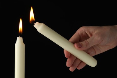 Photo of Woman lighting candle on black background, closeup