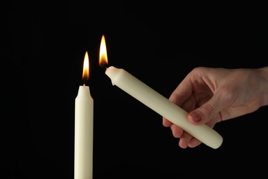 Photo of Woman lighting candle on black background, closeup