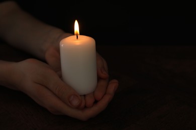 Photo of Woman holding burning candle at wooden table, closeup. Space for text