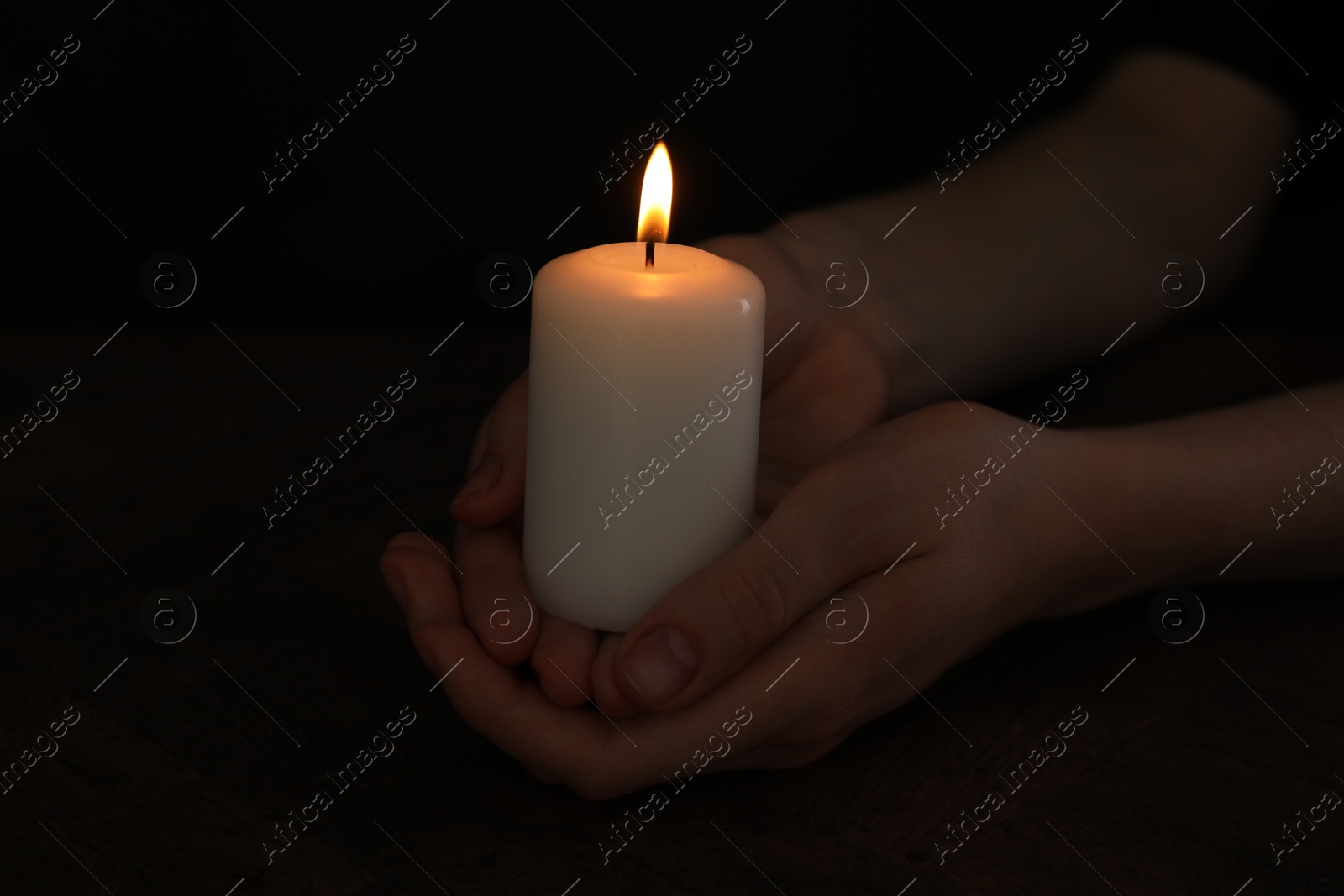 Photo of Woman holding burning candle at wooden table, closeup