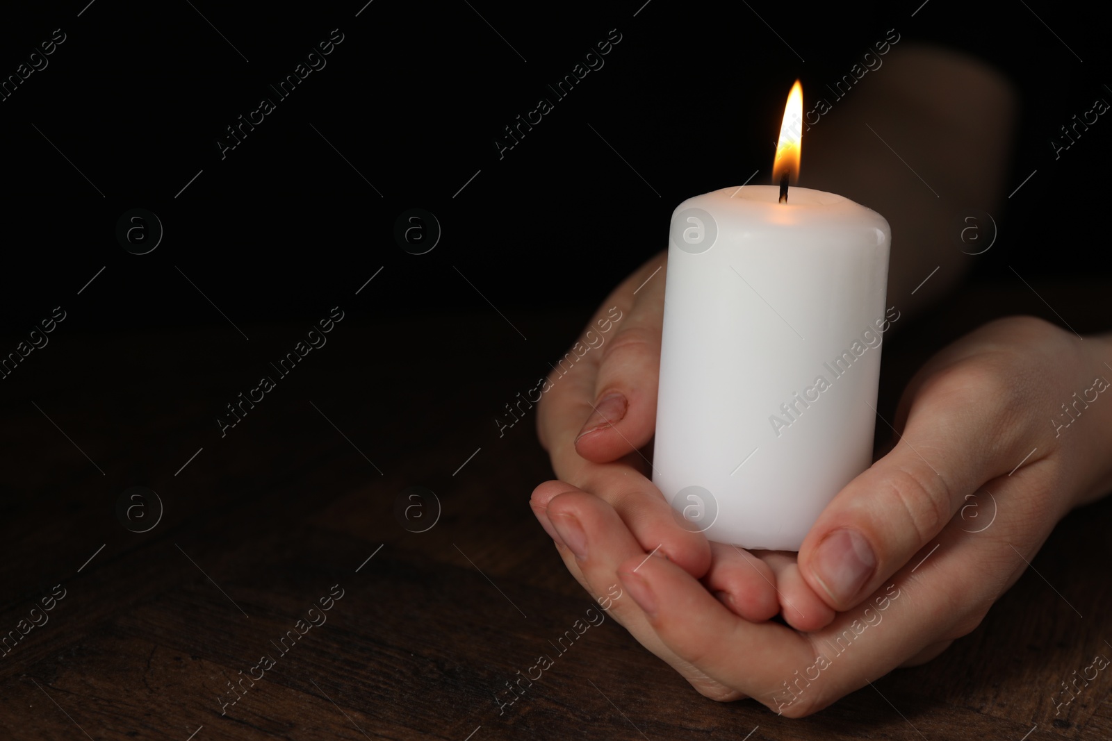 Photo of Woman holding burning candle at wooden table, closeup. Space for text