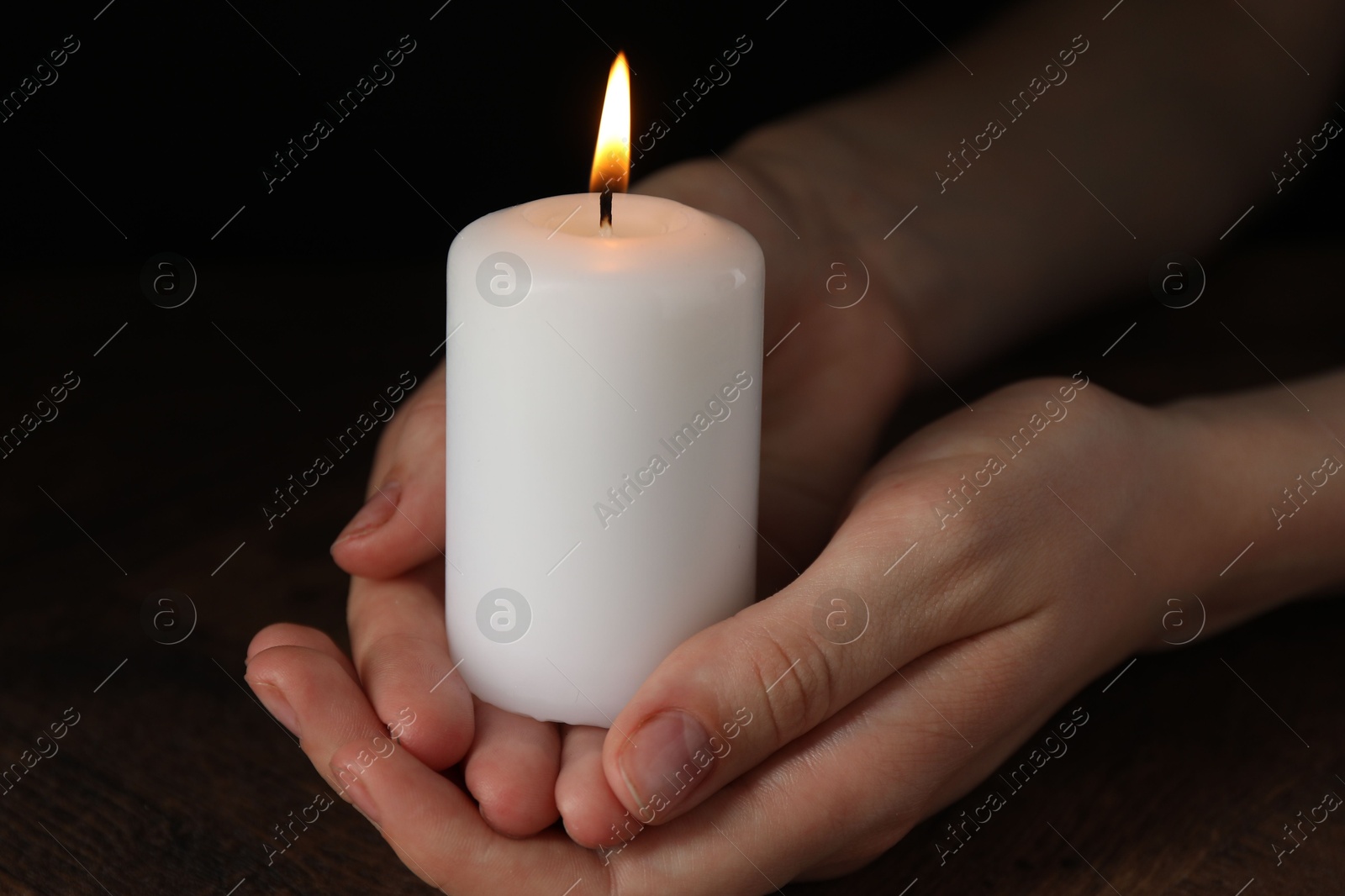 Photo of Woman holding burning candle at wooden table, closeup