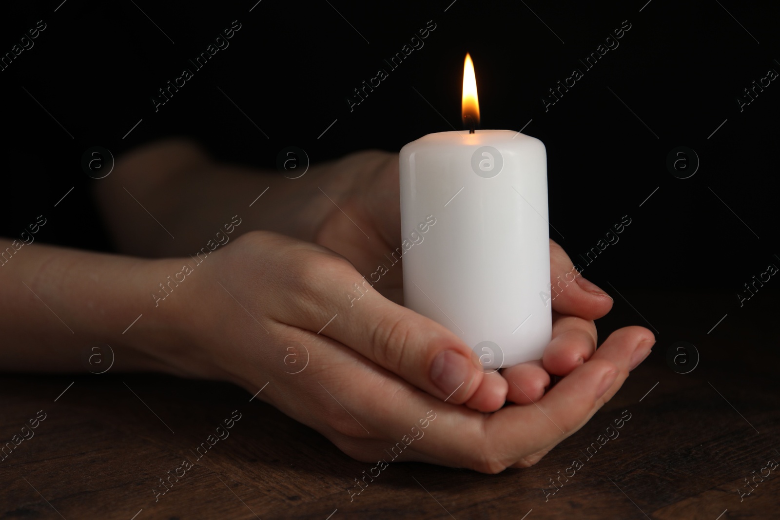 Photo of Woman holding burning candle at wooden table, closeup