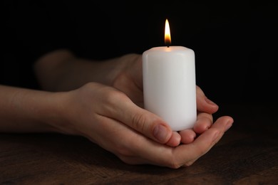 Photo of Woman holding burning candle at wooden table, closeup