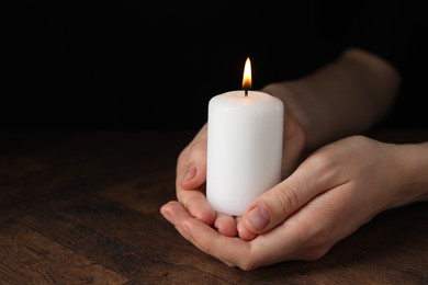 Photo of Woman holding burning candle at wooden table, closeup