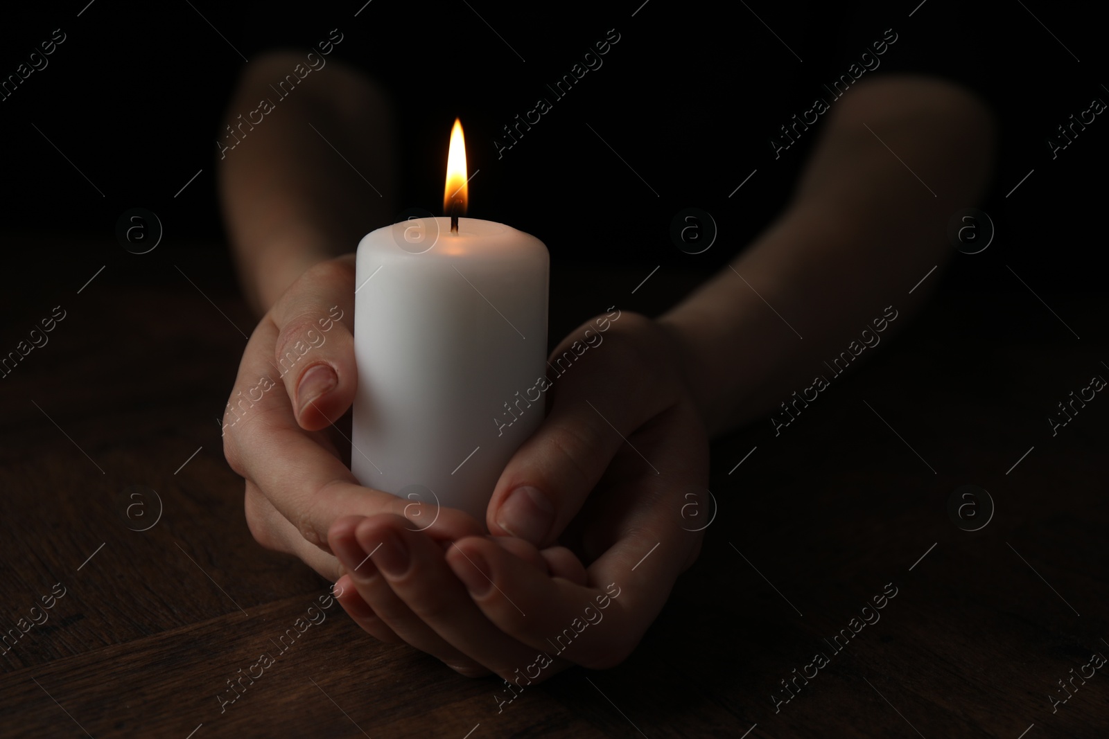 Photo of Woman holding burning candle at wooden table, closeup