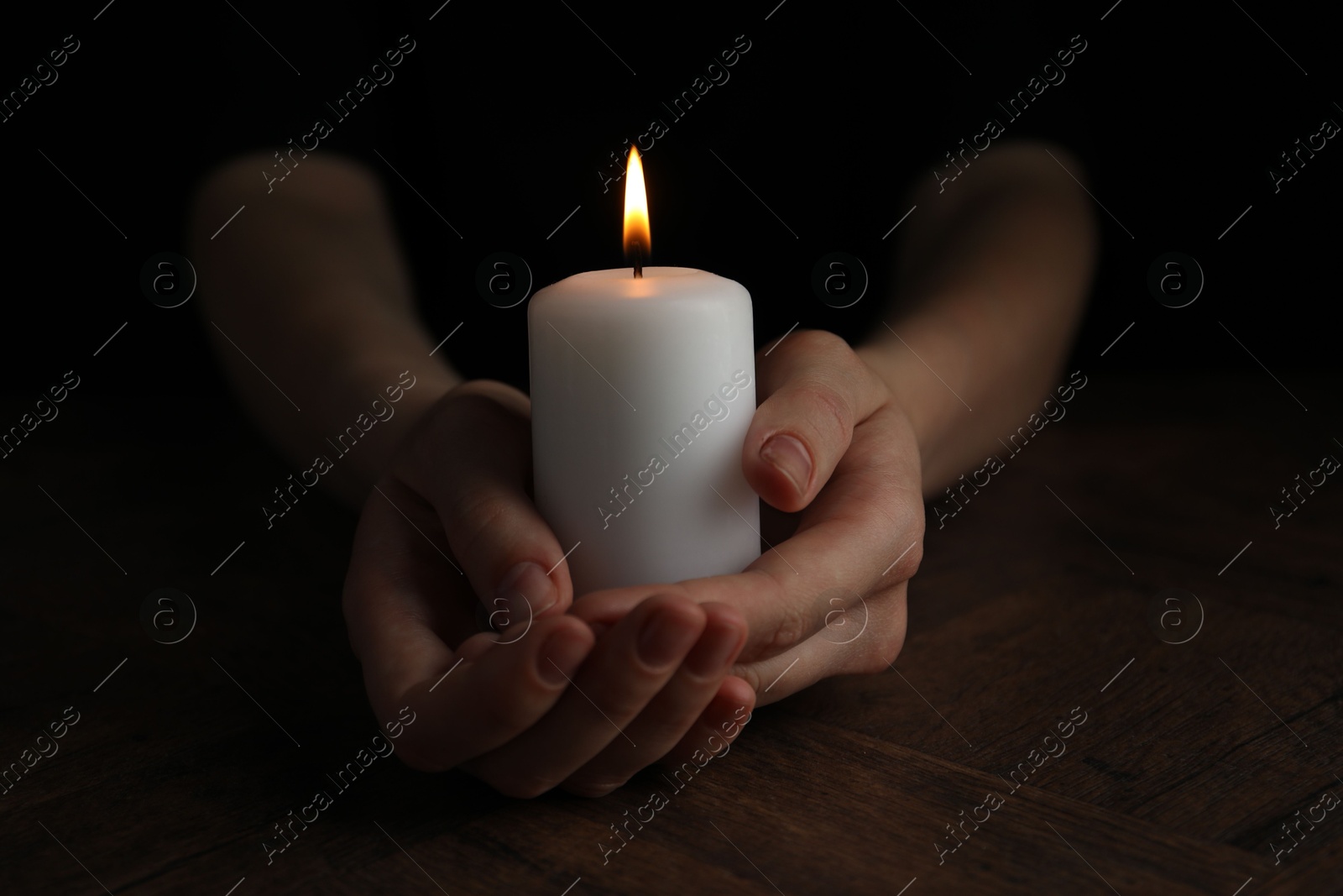 Photo of Woman holding burning candle at wooden table, closeup