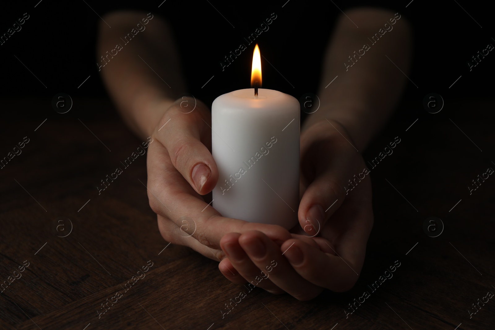 Photo of Woman holding burning candle at wooden table, closeup