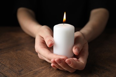 Photo of Woman holding burning candle at wooden table, closeup