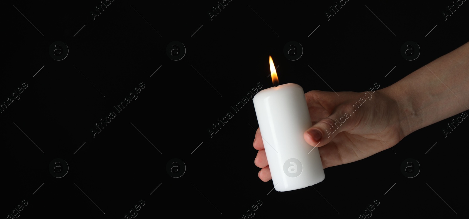 Photo of Woman holding burning candle on black background, closeup. Space for text. Banner design
