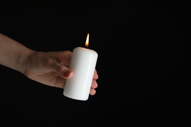 Woman holding burning candle on black background, closeup. Space for text