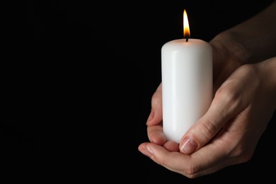 Woman holding burning candle on black background, closeup. Space for text