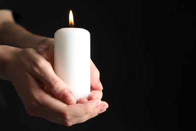 Woman holding burning candle on black background, closeup. Space for text