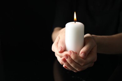 Photo of Woman holding burning candle on black background, closeup. Space for text