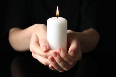 Photo of Woman holding burning candle on black background, closeup