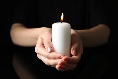 Woman holding burning candle on black background, closeup