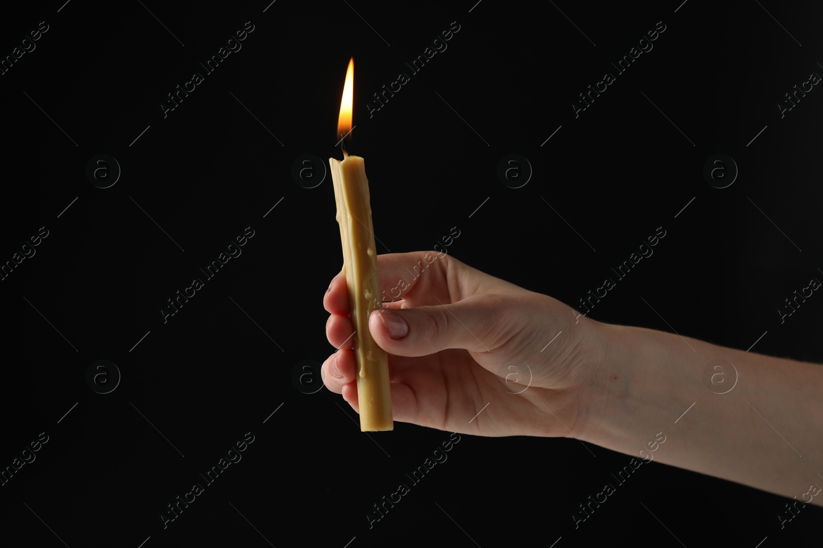 Photo of Woman holding burning church candle on black background, closeup