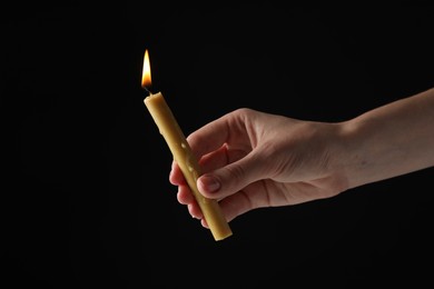 Photo of Woman holding burning church candle on black background, closeup