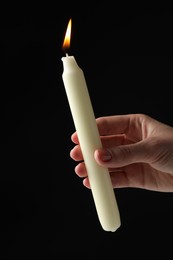 Woman holding burning candle on black background, closeup